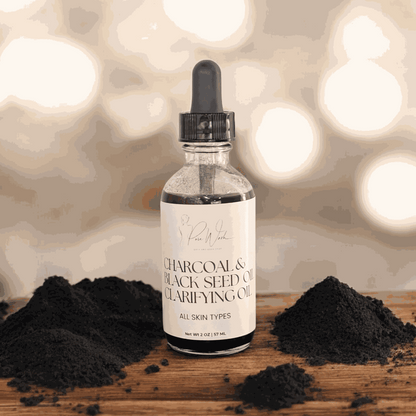 Charcoal & Black Seed Clarifying Oil bottle with powdered charcoal on wooden surface, all skin types.